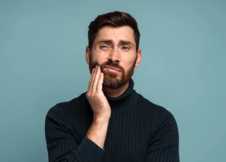 Man in black sweater holding his cheek in pain